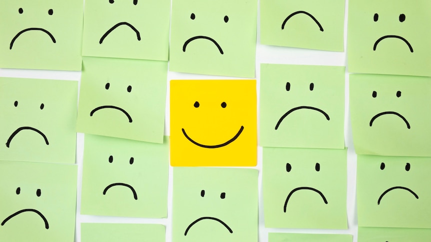 green sticky notes with sad faces and one yellow sticky note with happy face in centre