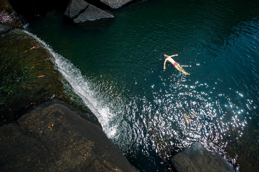 A man floats on his back in a calm waterhole surrounded by huge boulders.