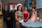 A family dressed in 1950s clothes stand in a 1950s style kitchen.