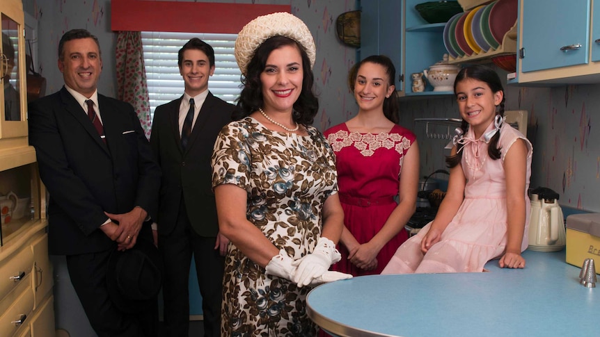 A family dressed in 1950s clothes stand in a 1950s style kitchen.