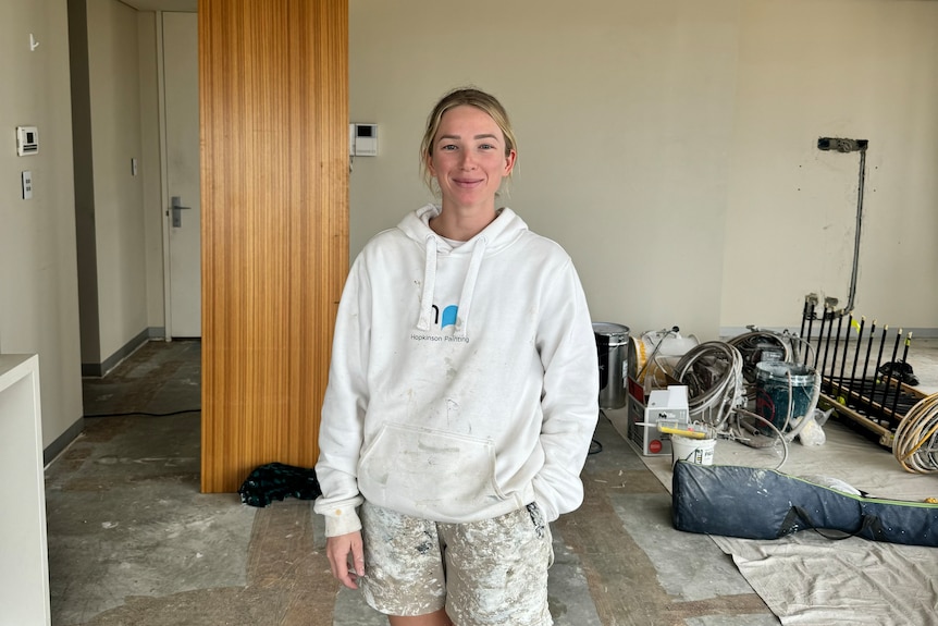 A young woman in paint covered clothes at a home under renovation. 