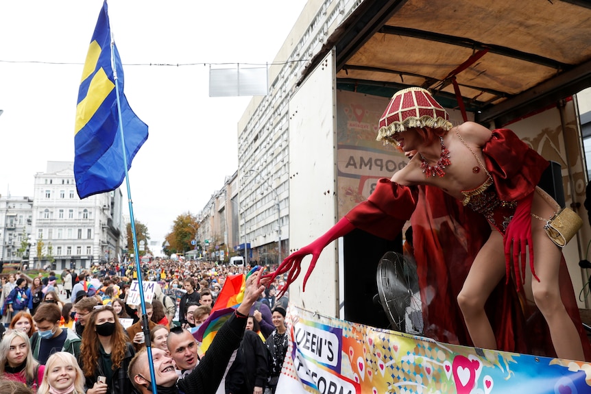 A man in costume on a float reaches out to someone in the crowd taking part in Kyiv's pride march.  