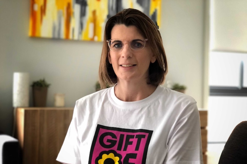 A woman sits and smiles into the camera, wearing an organ donation t-shirt.