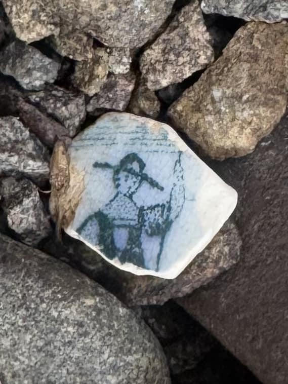 close up of ceramic fragment found on Bruny Island. Shows person in uniform wearing hat.
