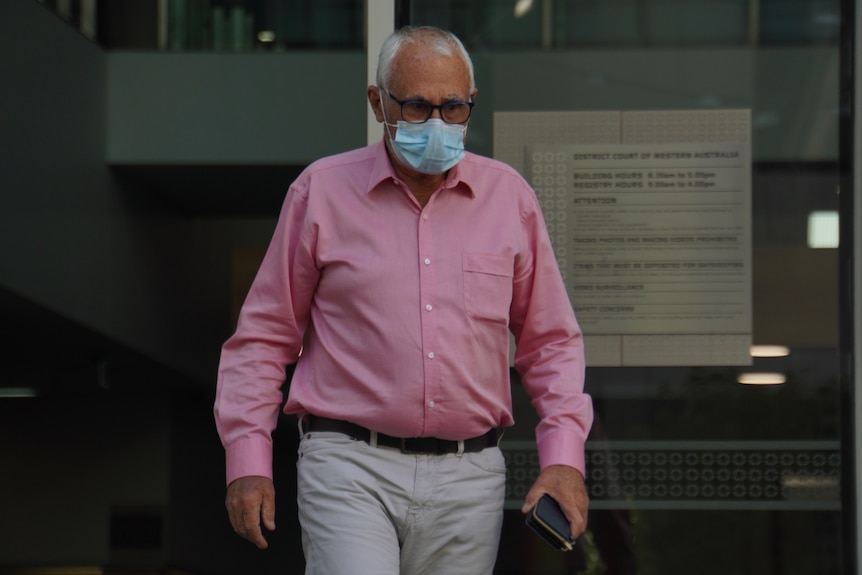 A man wears a pink shirt and khaki pants as he leaves court