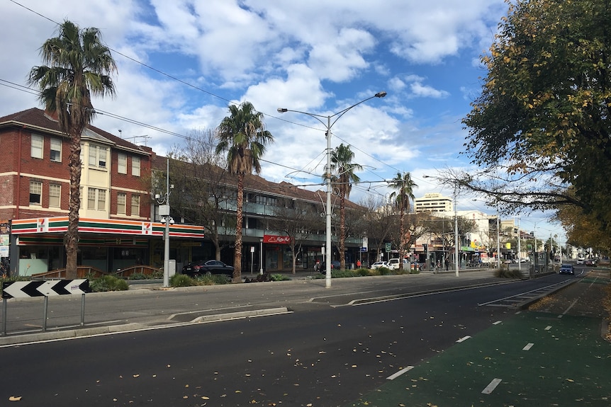 A photo of Fitzroy Street in St Kilda showing the road, tram tracks and shopping strip.