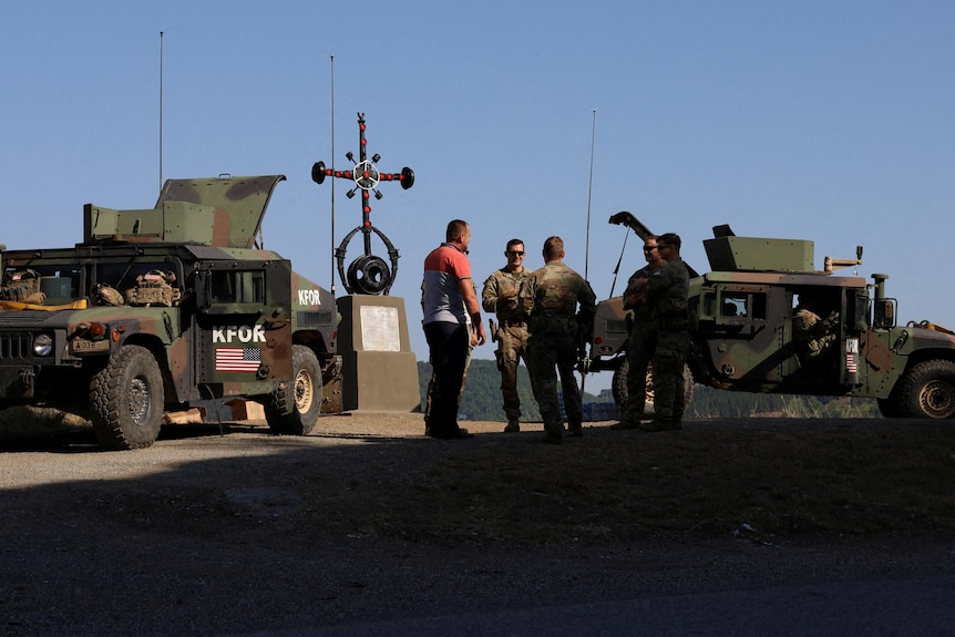 Four US soldiers stand outside of two military vehicles.