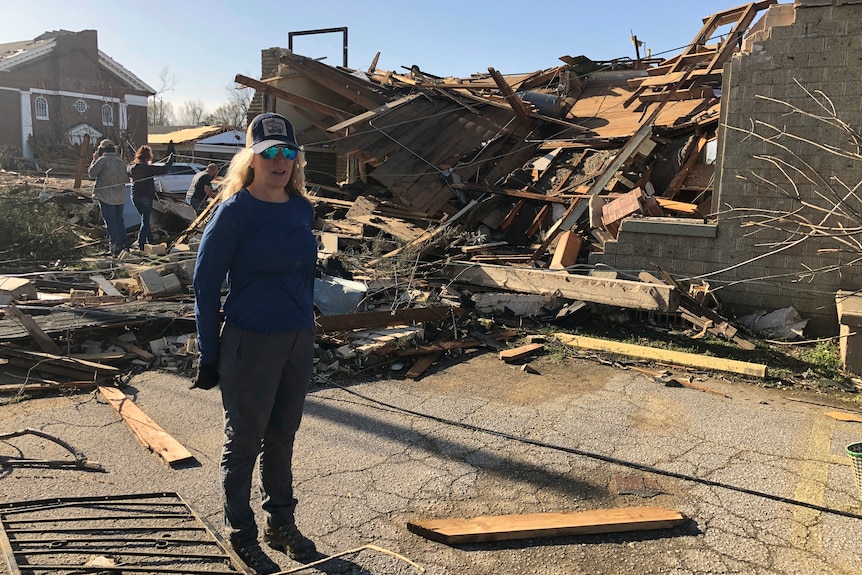 A woman stands in from of a damaged building.