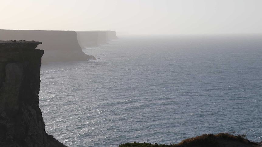 Large sea cliffs stand on a foggy morning in clam waters.