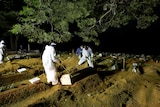 Cemetery workers wearing protective clothing bury a person at night in a cemetery.