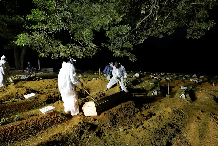 Cemetery workers wearing protective clothing bury a person at night in a cemetery.