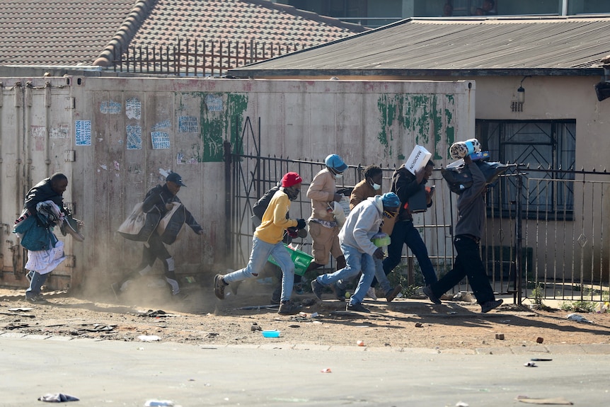 People run with looted goods through a dusty street in South Africa.