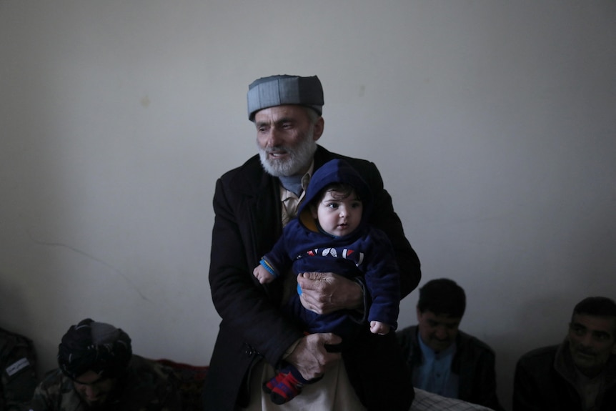 Baby Sohail's grandfather holds him, standing in Mr Safi's house in Kabul, January 8, 2022.