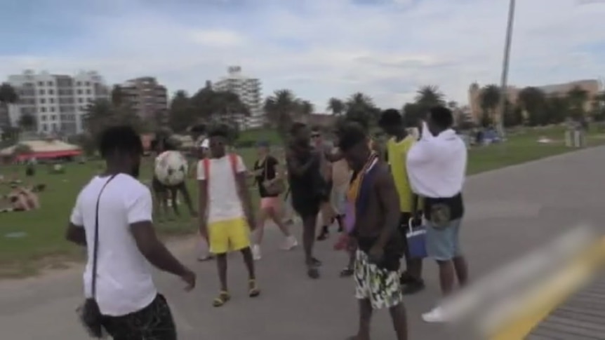 Young men kick around a soccer ball on the footpath next to the beach.