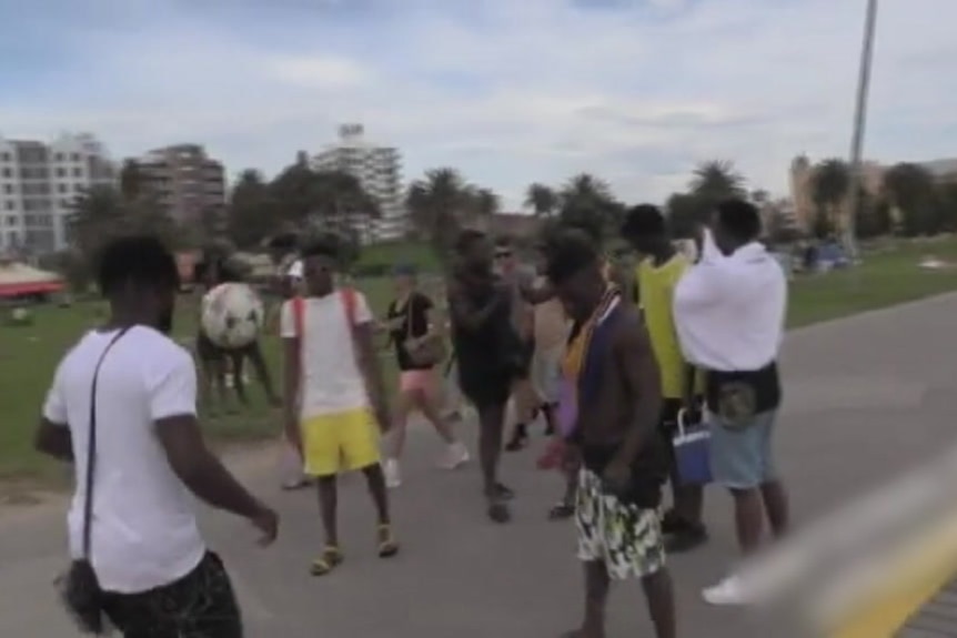 Young men kick around a soccer ball on the footpath next to the beach.