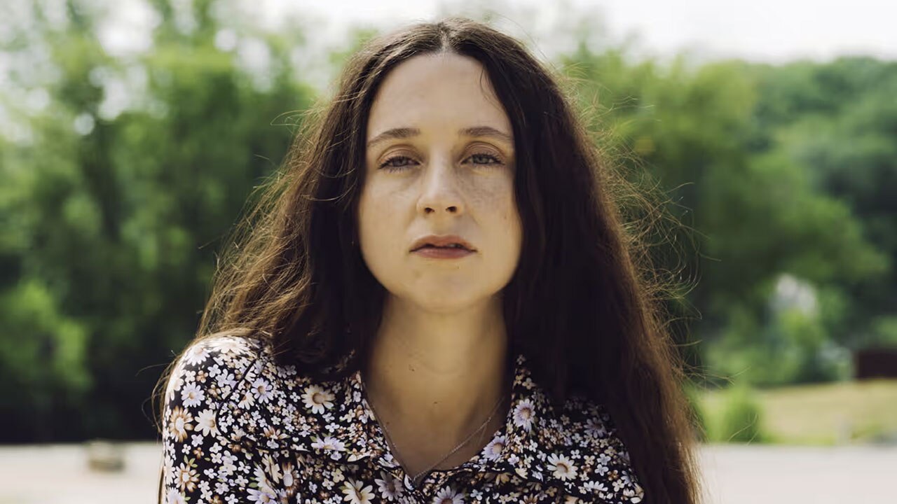 photo portrait of Waxhatchee's Katie Crutchfield wearing black and white dress, brown hair blowing gently in the wind