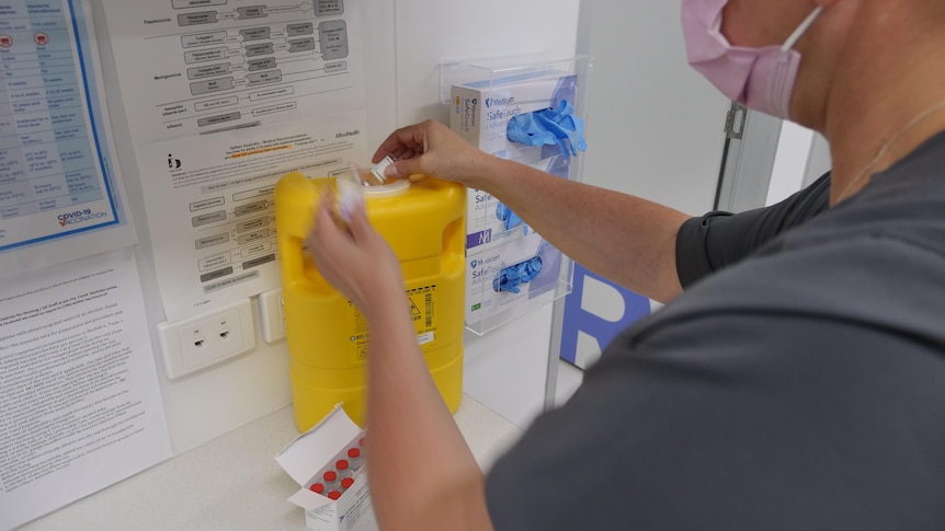 A nurse throws vaccines in a yellow medical bin