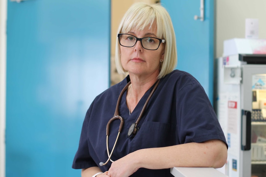 woman stands with hospital scrubs on in front of blue door in clinic