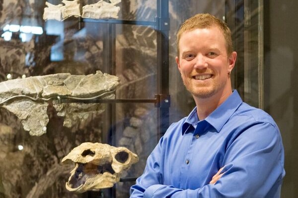 Man stands smiling in front of a cabinet of dinosaur bones