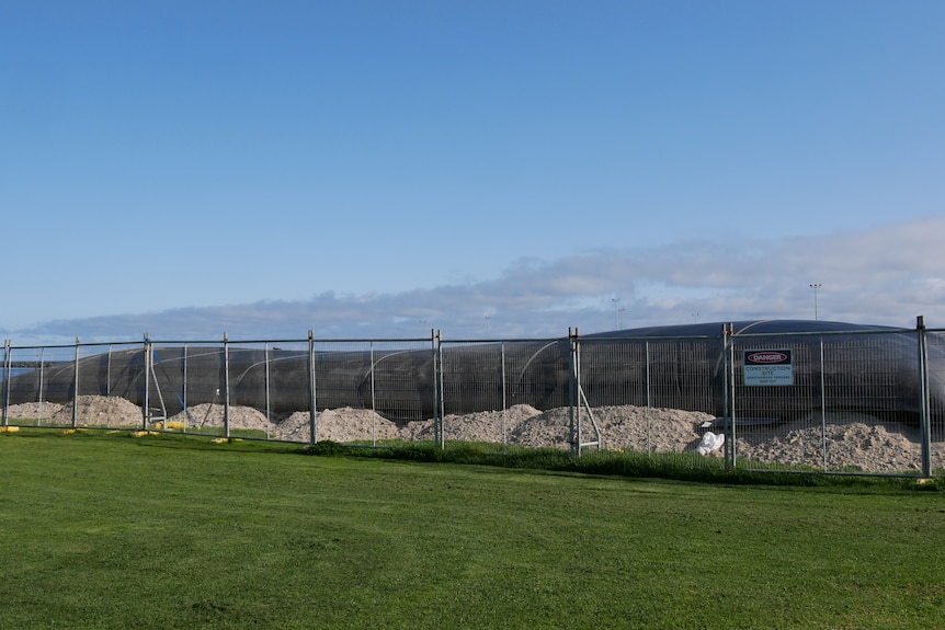Black bio bags (shaped like giant pillows) in background across entire screen with fence in front. Grass in foreground.