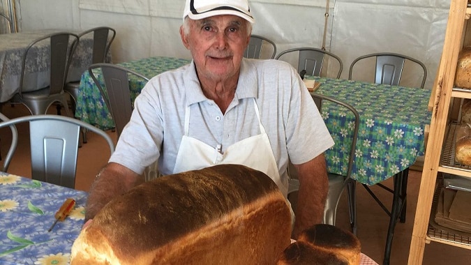 A retired baker sits behind of a loaf of bread he has baked.
