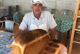 A retired baker sits behind of a loaf of bread he has baked.