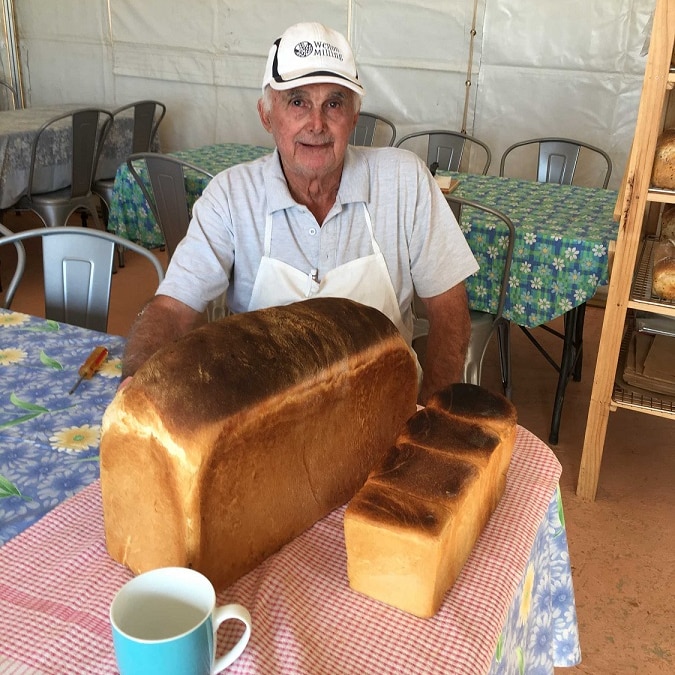 A retired baker sits behind of a loaf of bread he has baked.