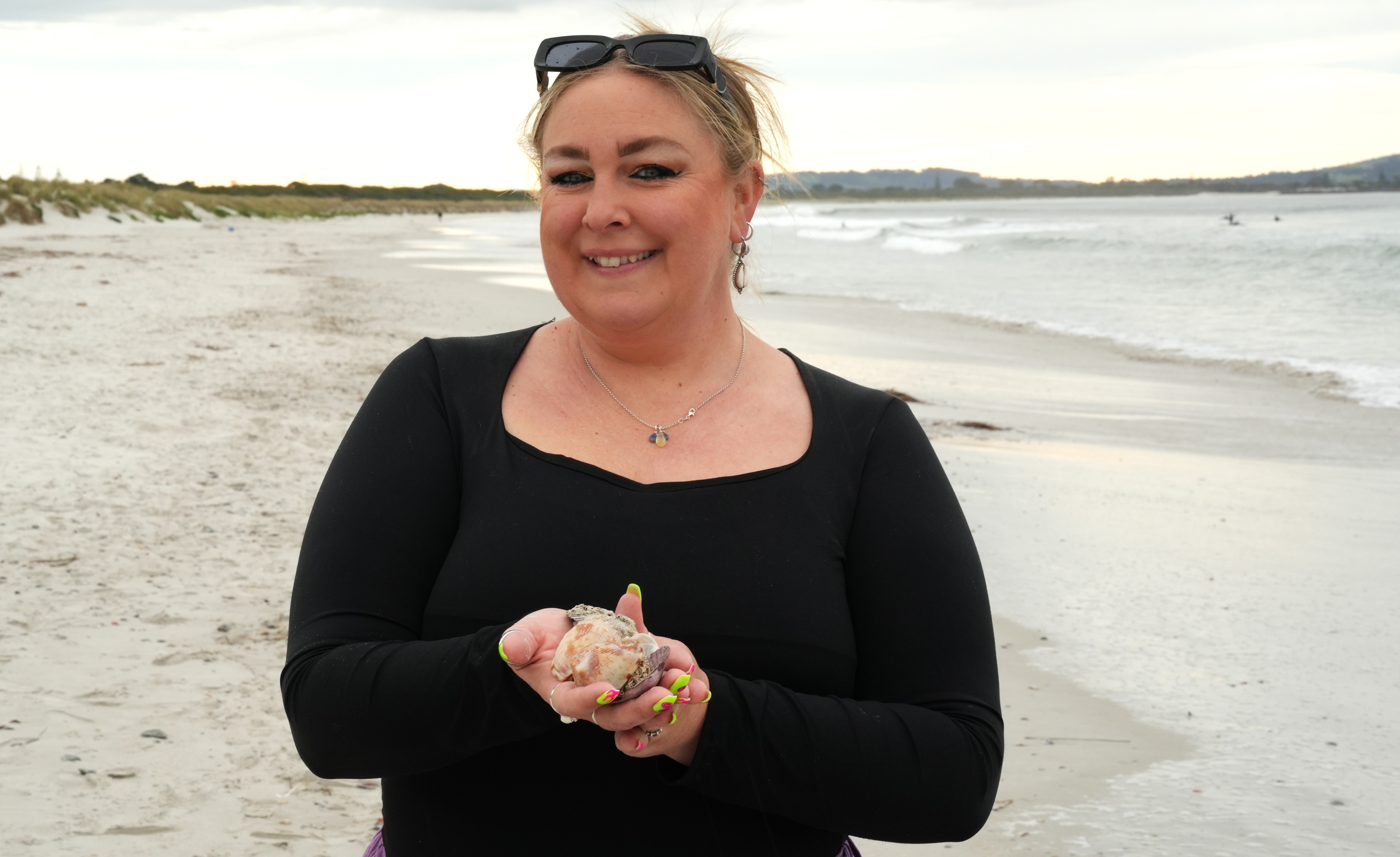 A woman on the beach holding shells in her hand and ocean in background