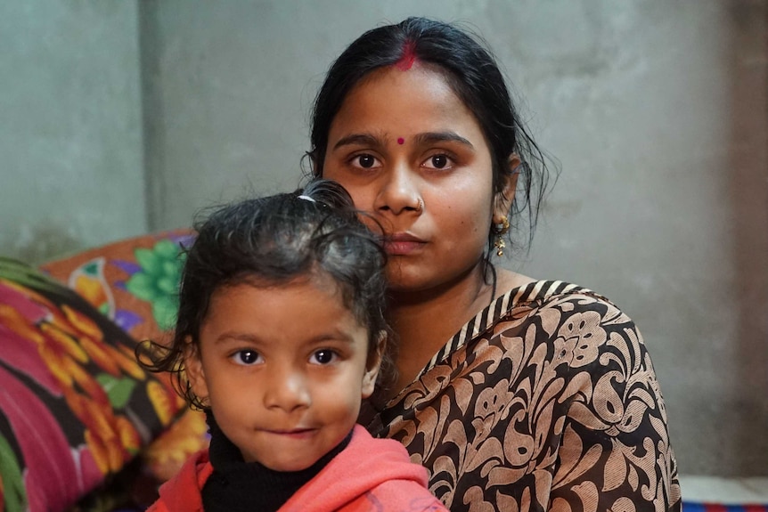 Babli Singh sits with her daughter on a bed in their home in Delhi.