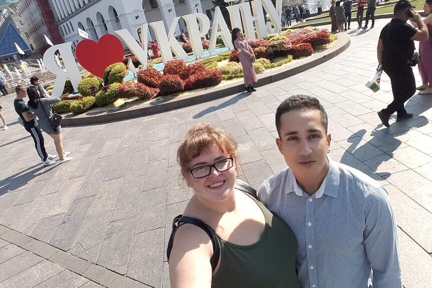 A couple pose for a loving selfie in a city square.