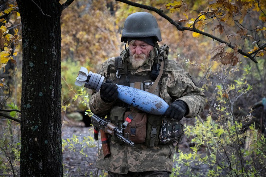 A soldier in the bush holds a blue shell with hand writing on it.