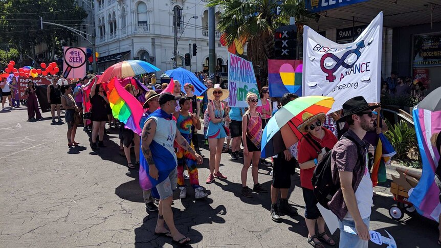 Marchers in the Midsumma Pride March with rainbow umbrellas and signs.