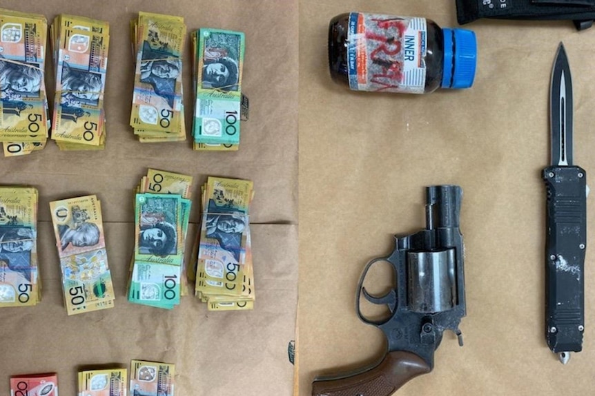 Queensland police display bundles of cash, a gun, knife and drugs on a table.