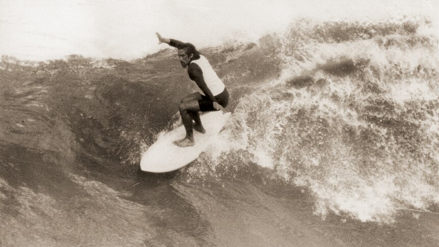 A black and white photo of a man surfing a large wave.