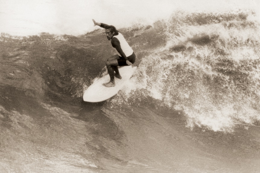 A black and white photo of a man surfing a large wave.