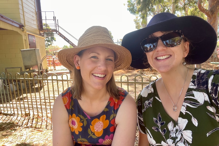 Two women in hats and flowery tops smiling, one wearing her sunglasses.
