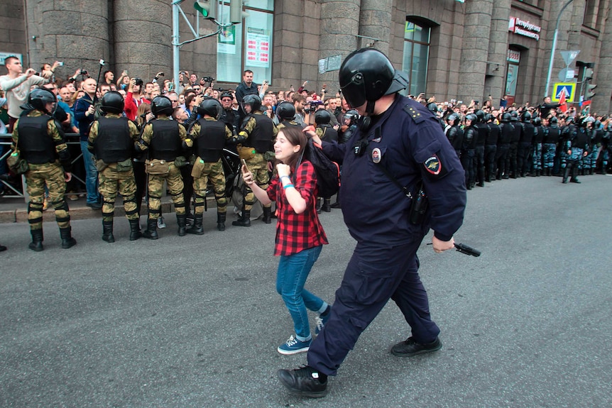 A Russian police officer detains a teenager during rally.