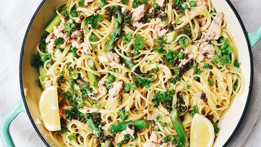 A pan of one pot spaghetti with parsley, capers, tuna, lemon, peas and asparagus, illustrating our recipe.