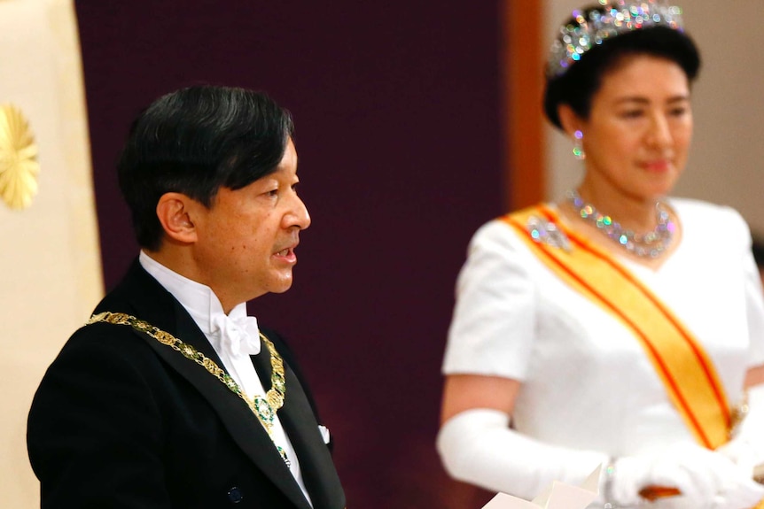 Japanese Emperor Naruhito, standing next to Empress Masako, reads his first address from a piece of paper.