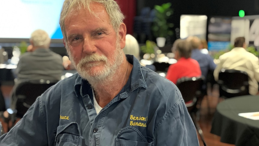 Bruce Benson sitting at a table, people behind him.