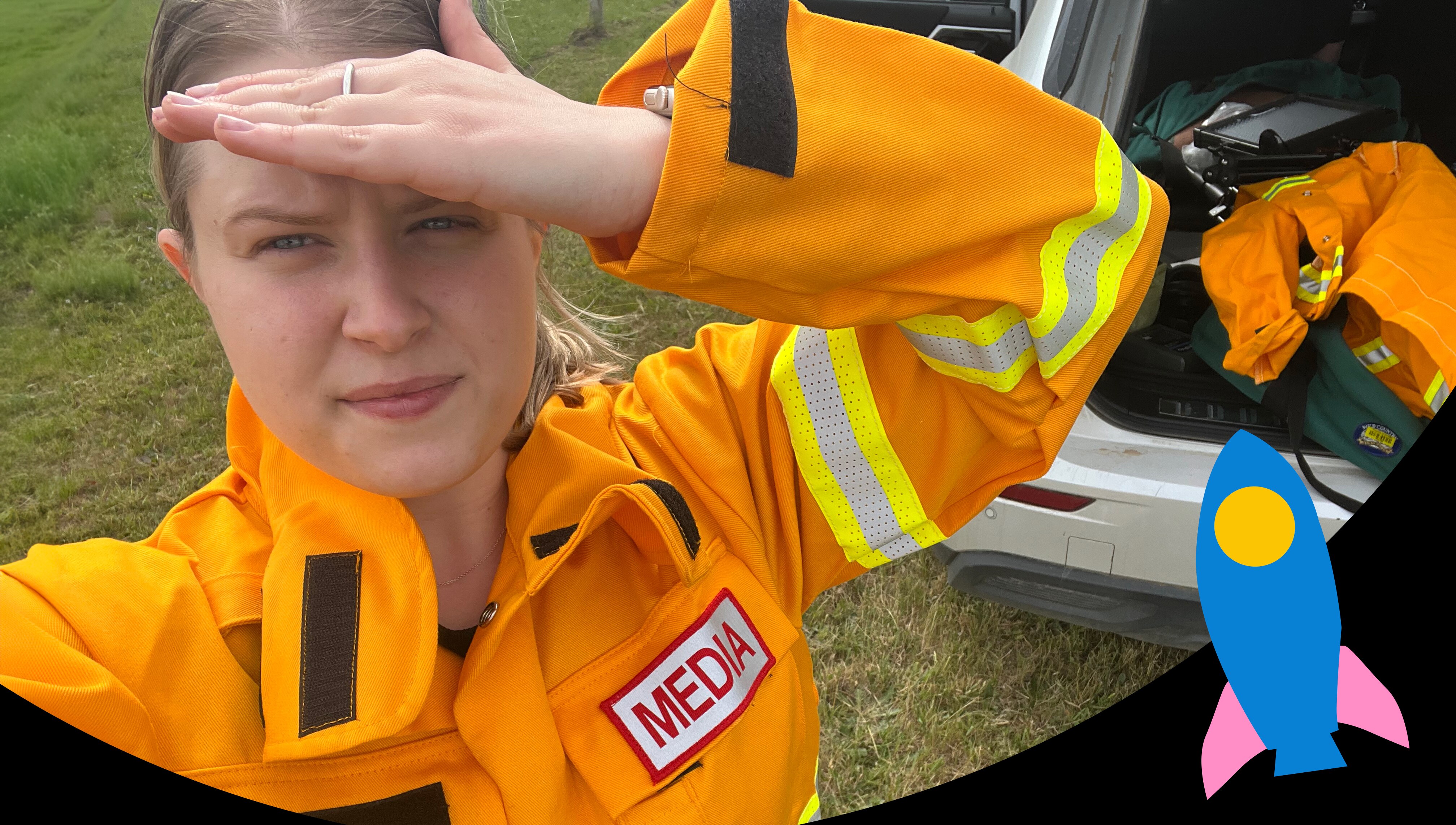 Young woman in orange emergency protective clothing. She has a media patch on the pocket.
