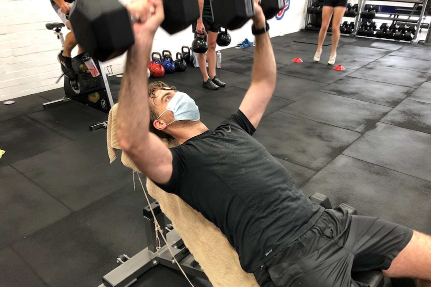A man lifts weights wearing a face mask at an F45 studio.