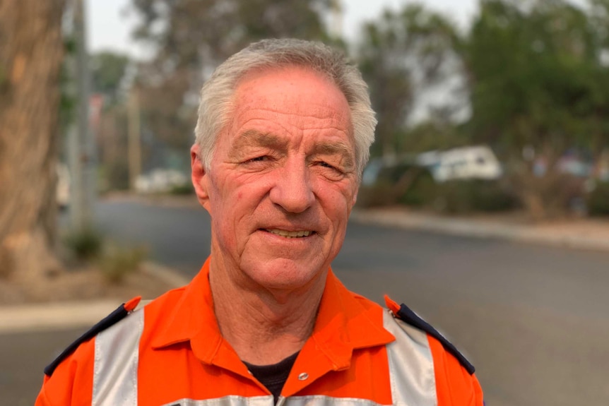 An older man with short light grey hair wearing a bright orange SES jacket. He's looking into the camera.