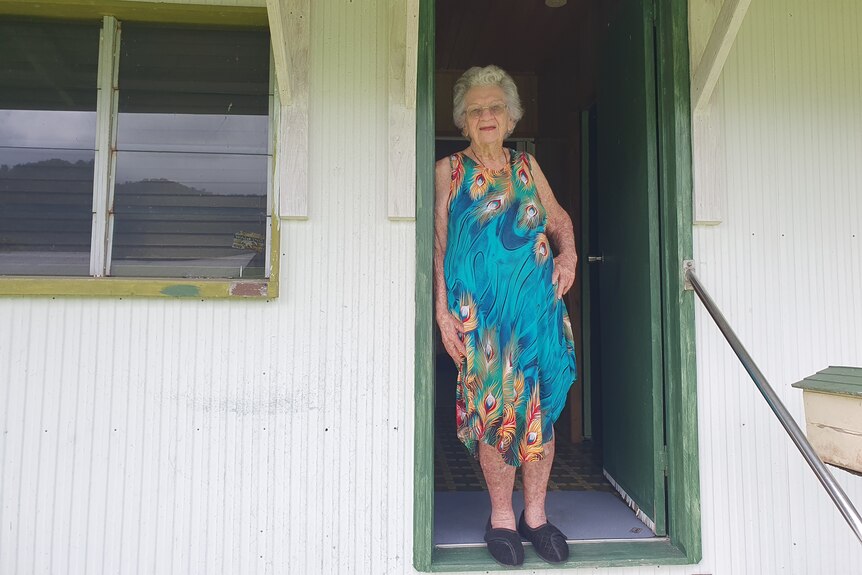 Older lady in blue dress standing in doorway of house