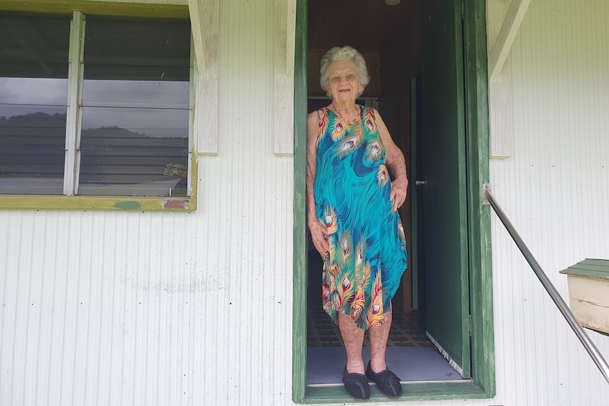 Older lady in blue dress standing in doorway of house