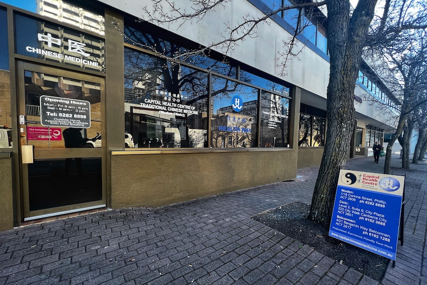 The outside of a shopfront with window decals that read "Capital Health Centre of Traditional Chinese Medicine (Woden Clinic)".