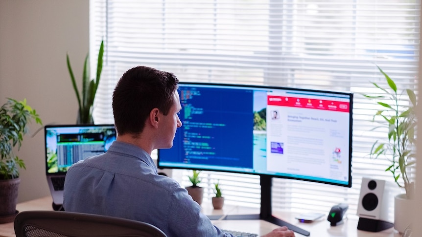 A man sitting at his computer with a wide screen.