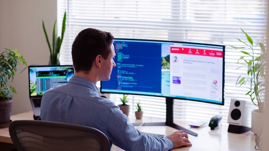 A man sitting at his computer with a wide screen.