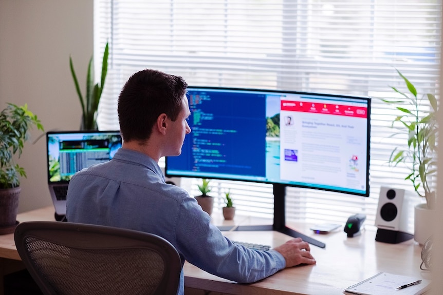 A man sitting at his computer with a wide screen.