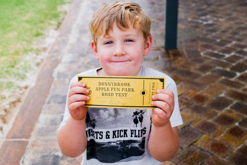 A boy smiling and looking at the camera with a golden ticket